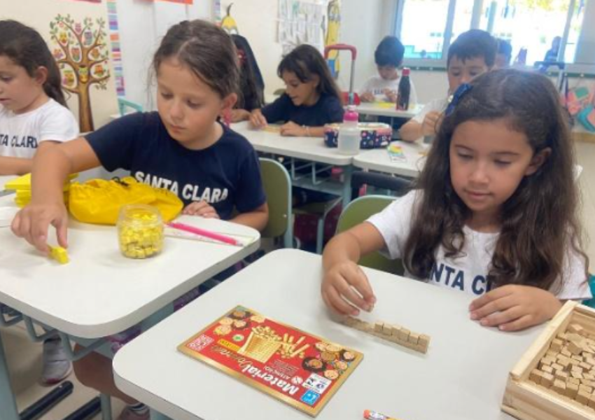 A foto mostra crianças estudando com material dourado.